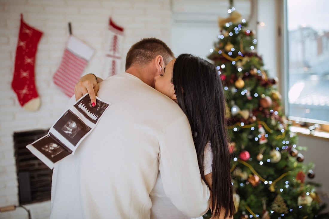 couple holding sonogram by christmas tree
