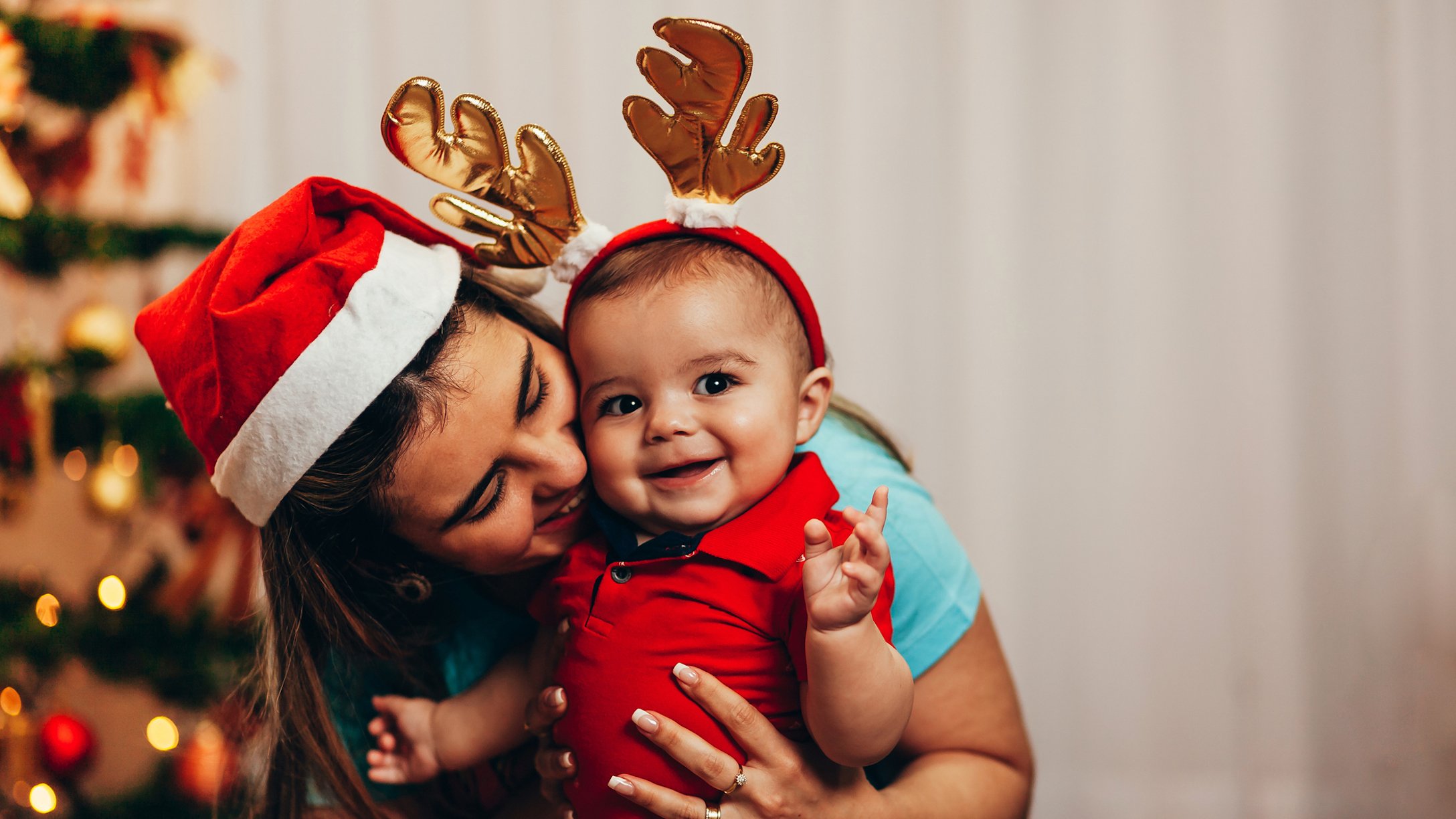 Mom kissing her baby wearing reindeer antlers