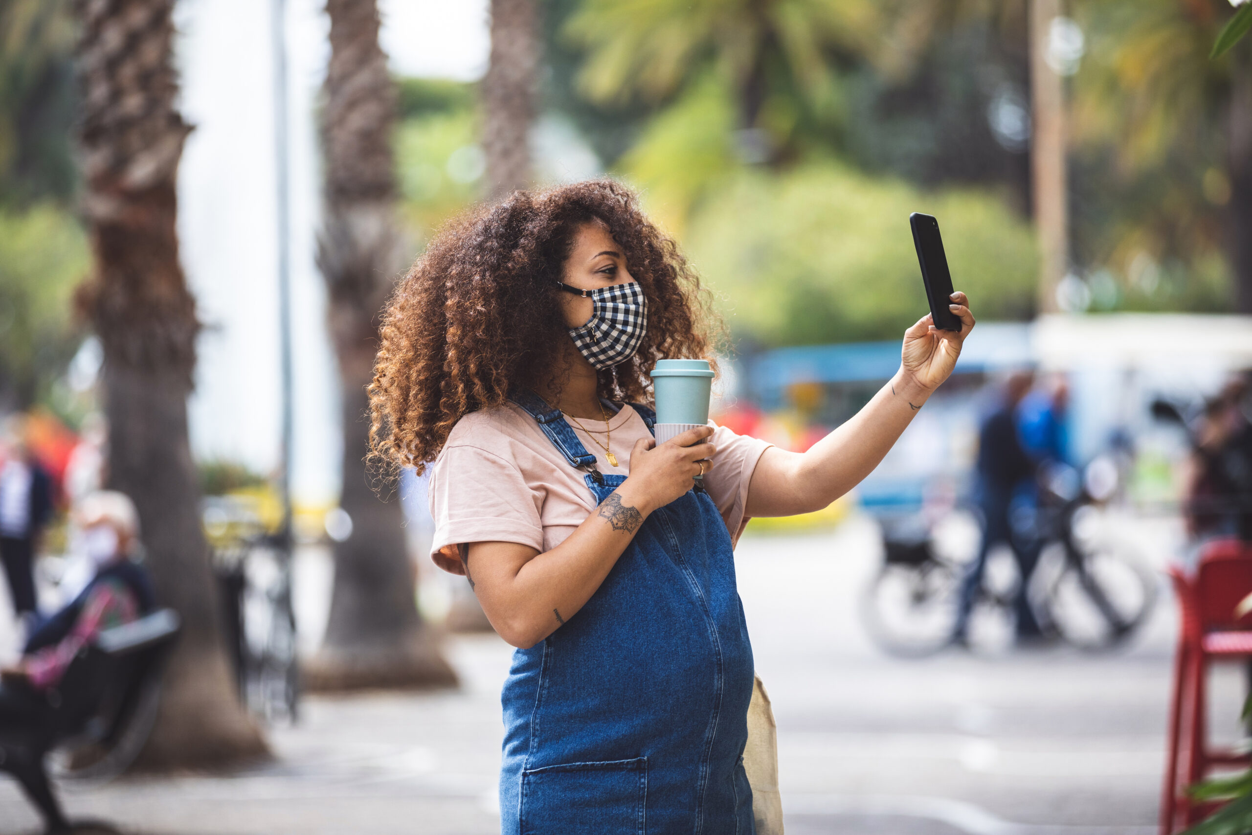 Pregnant woman walking in the city in a sunny day protecting herself with a cloth face mask