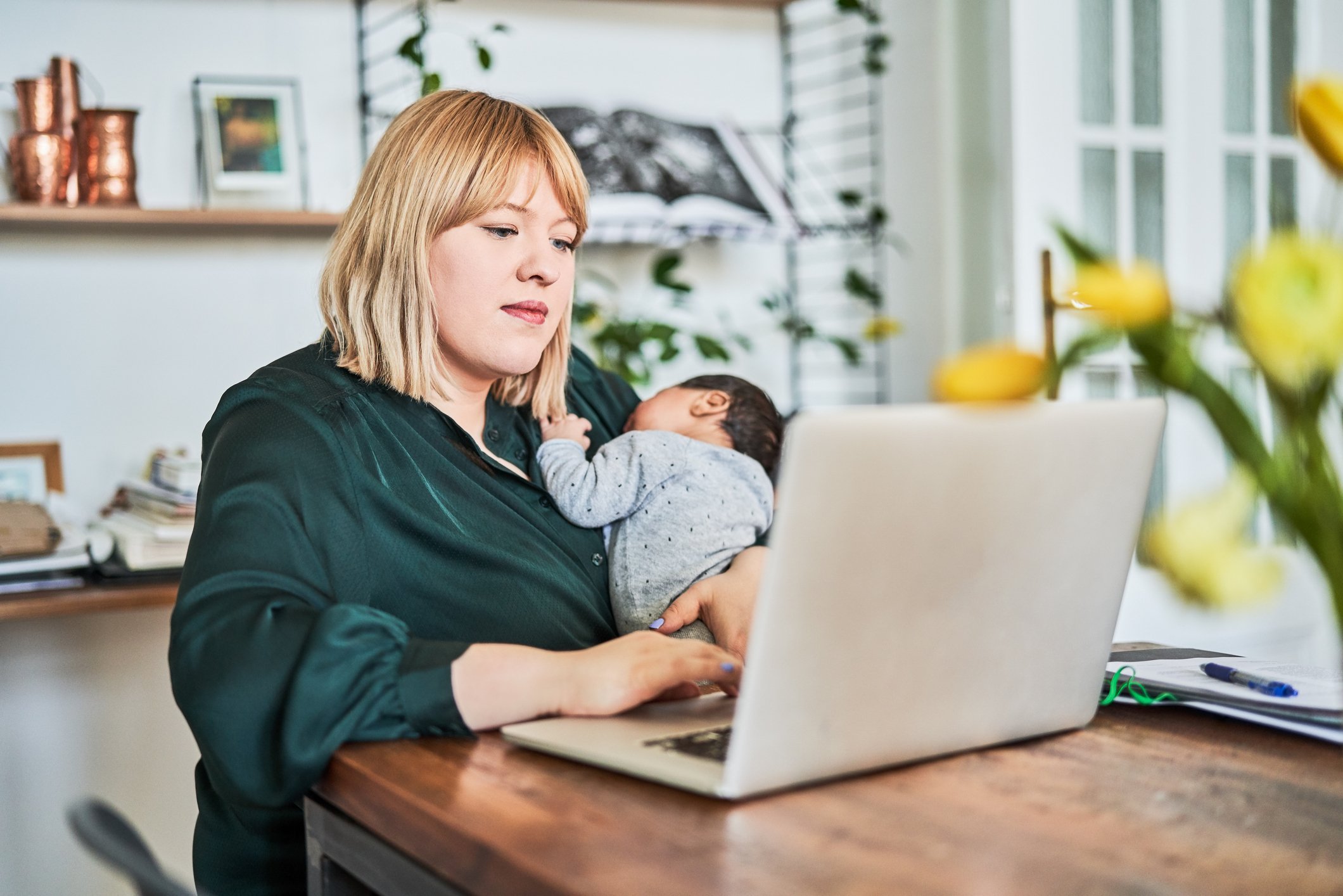new mom holding newborn baby and working on computer