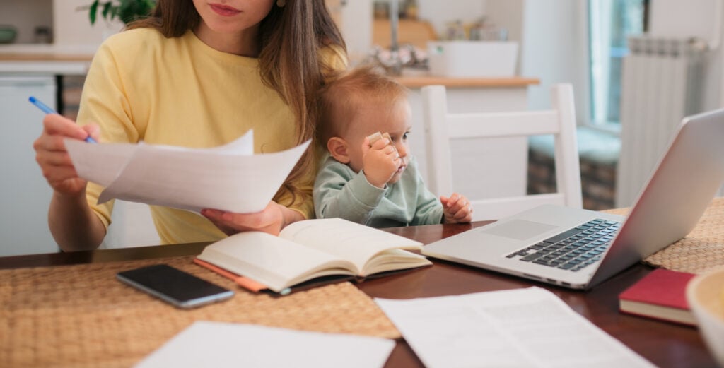 Young Caucasian mother taking her work home due to pandemic, working from home and taking care of her baby boy at the same time