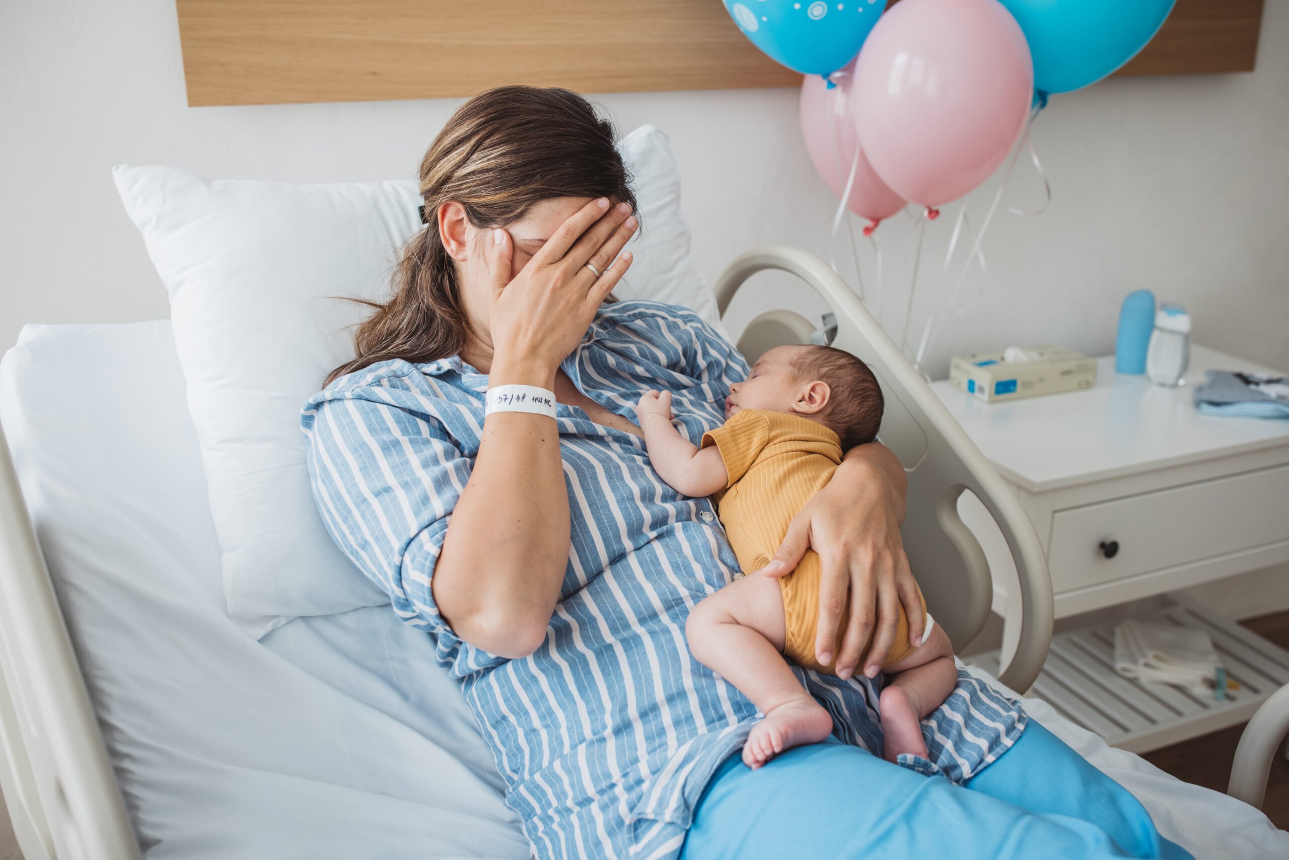 Mother holding new born baby at hospital bed.
