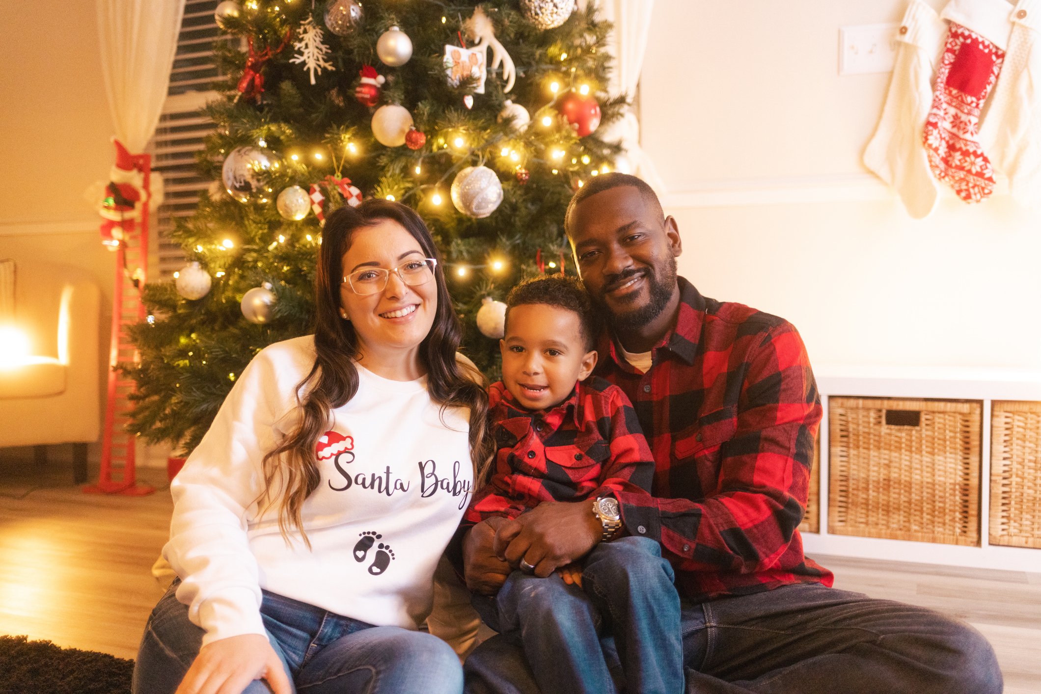 couple and son announcing mom is pregnant in front of a christmas tree