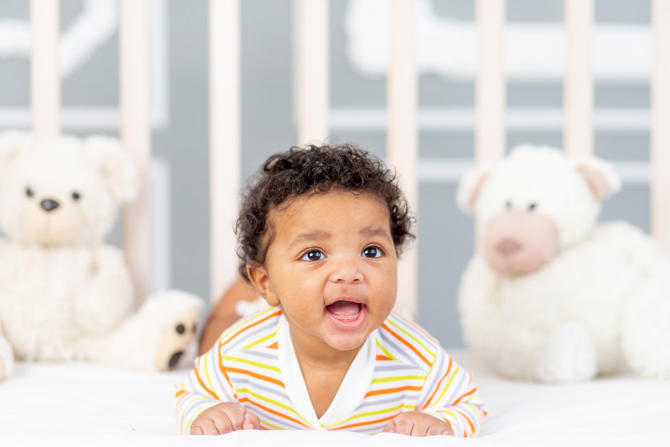African-American small child lying in bed in orange clothes with soft bears