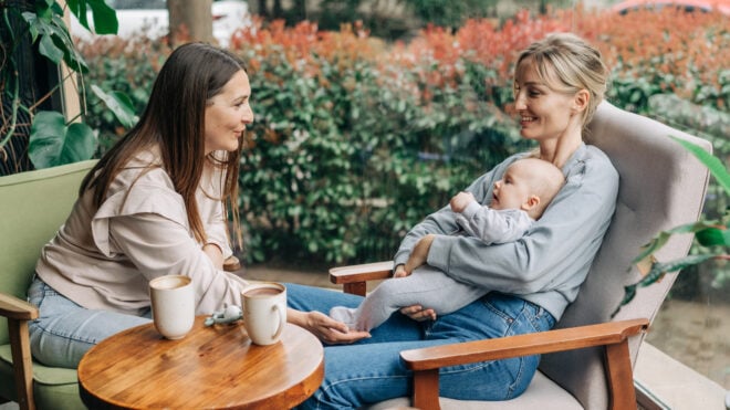 Two women talk about motherhood while nursing a baby while sitting in a cafe.