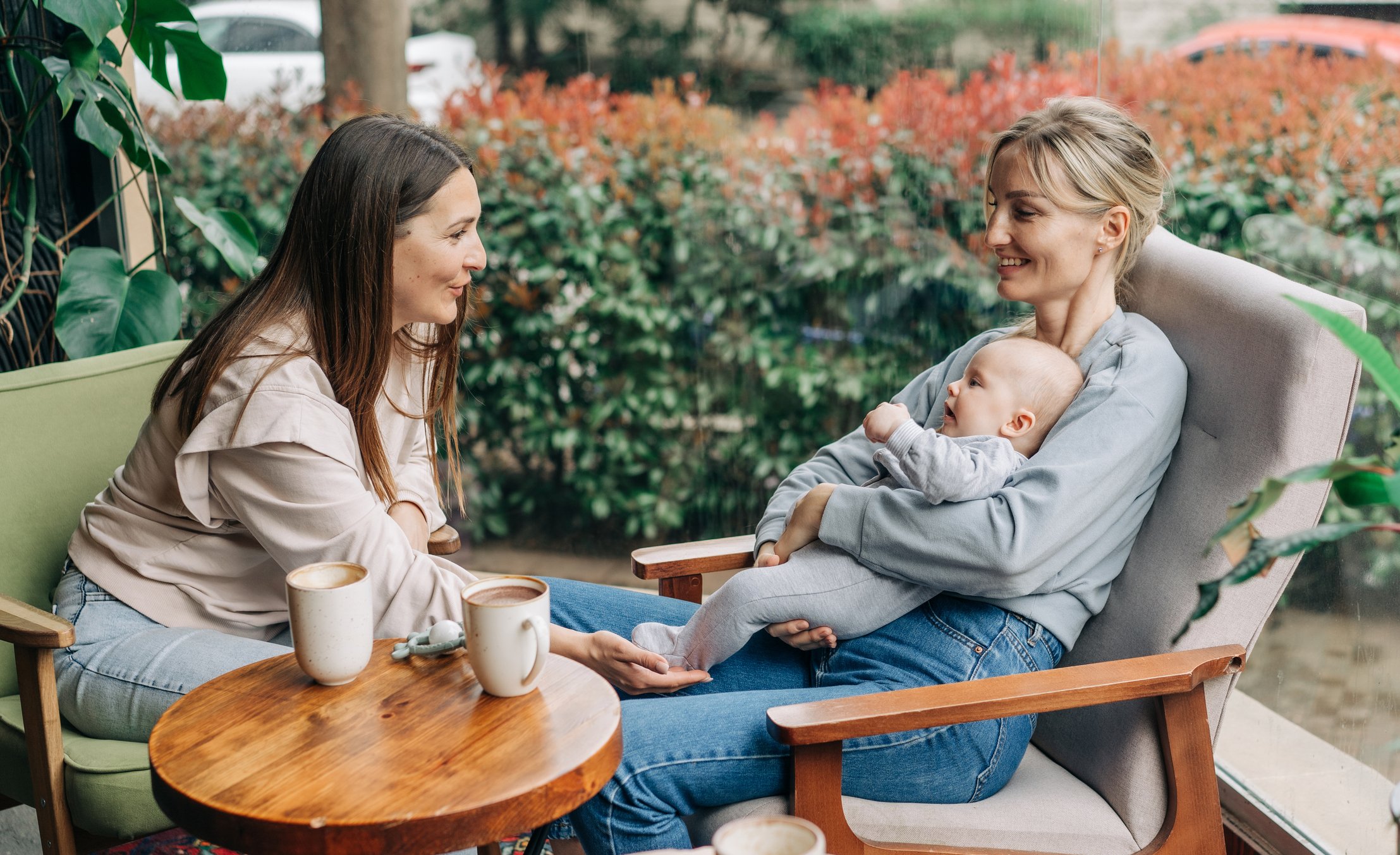 Two women talk about motherhood while nursing a baby while sitting in a cafe.