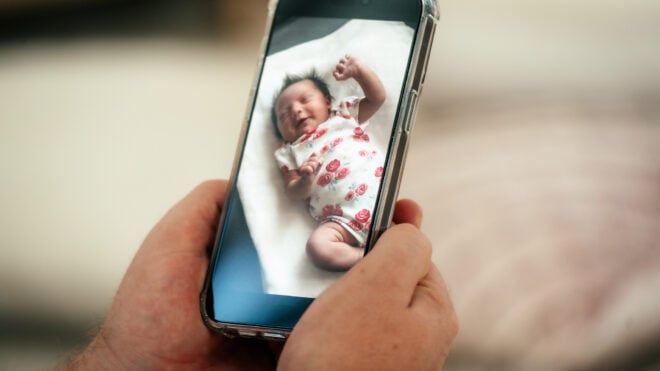 Father using newborn girl baby smart monitor on his mobile phone at home