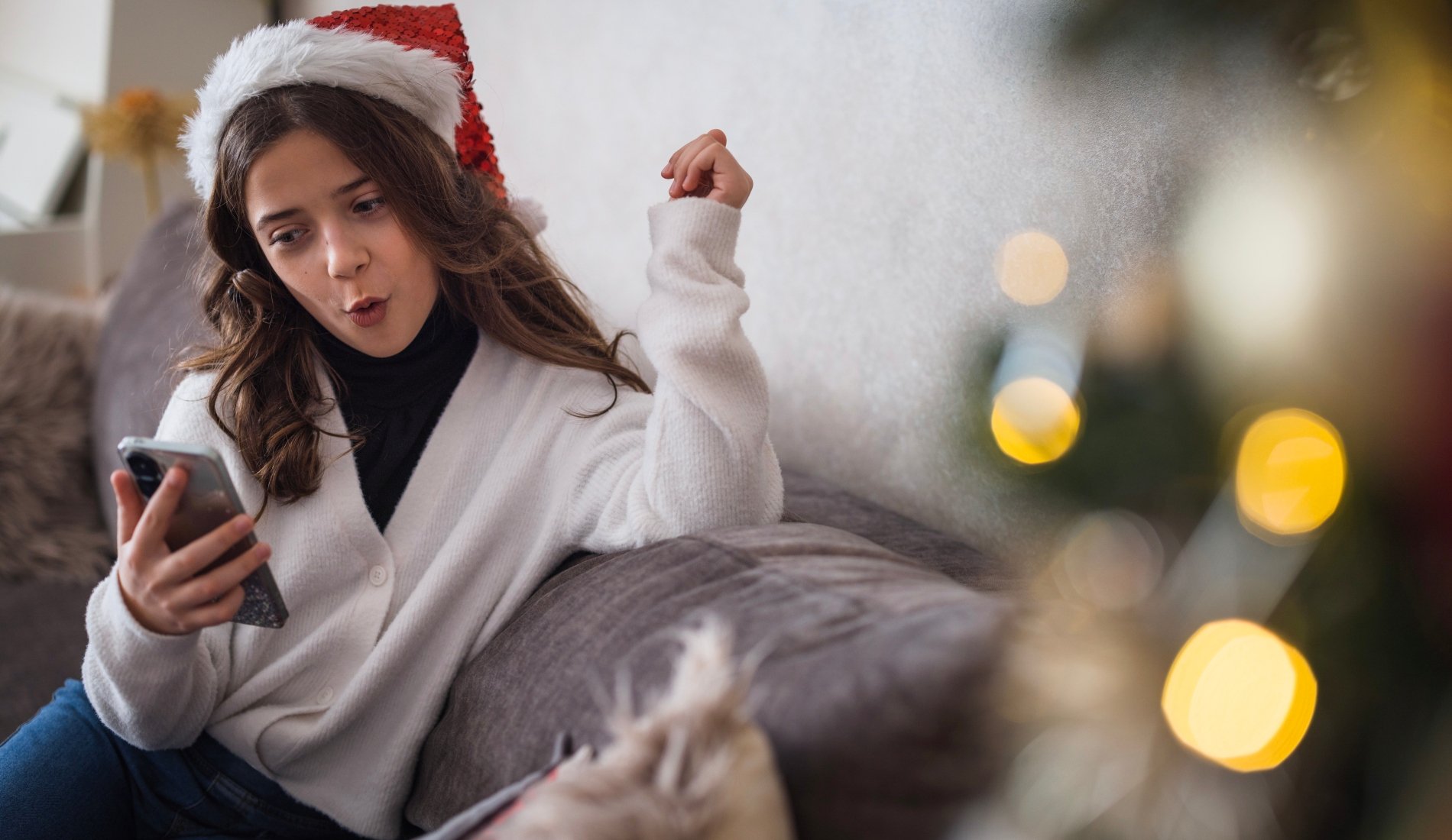 teen girl in a santa hat looking surprised at her phone